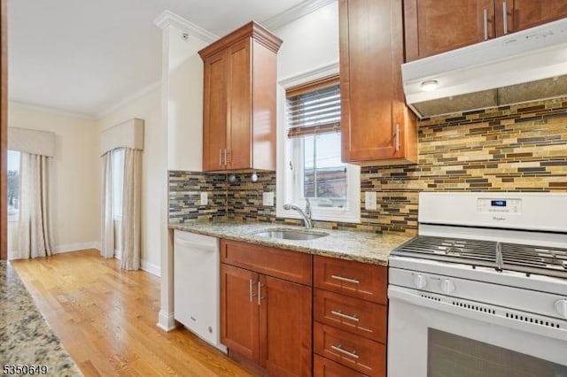 kitchen with white appliances, crown molding, light stone countertops, under cabinet range hood, and a sink