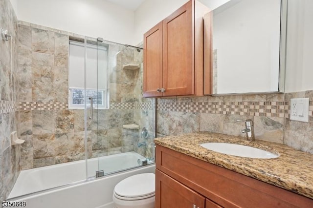 full bathroom featuring tasteful backsplash, toilet, vanity, and bath / shower combo with glass door