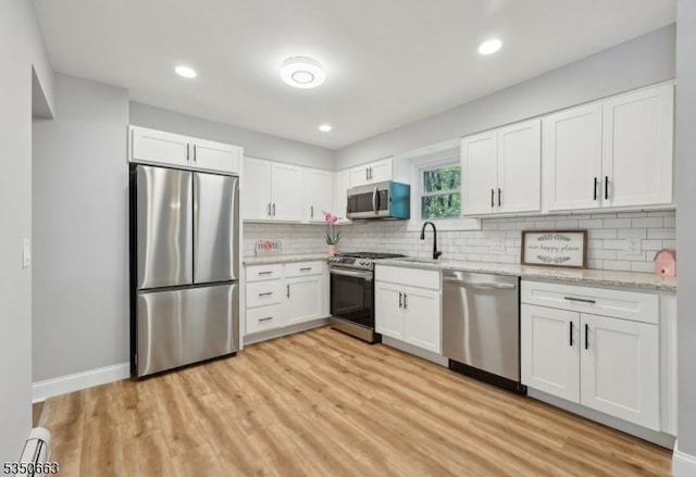 kitchen with light stone countertops, light wood finished floors, stainless steel appliances, white cabinetry, and decorative backsplash