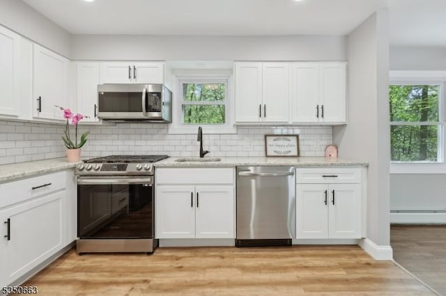 kitchen with stainless steel appliances, white cabinetry, a sink, and a baseboard radiator