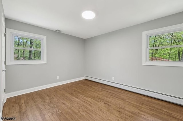 spare room featuring baseboards, plenty of natural light, baseboard heating, and wood finished floors