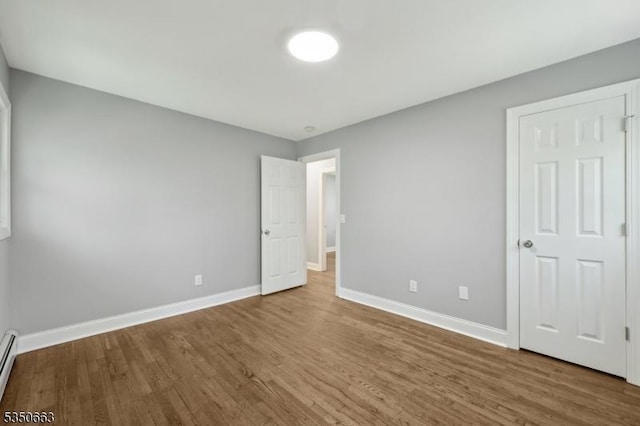 unfurnished bedroom with baseboards, a baseboard heating unit, and wood finished floors