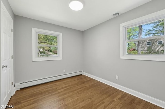 unfurnished bedroom featuring baseboards, wood finished floors, baseboard heating, and multiple windows