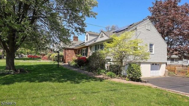 view of property exterior featuring fence, roof mounted solar panels, aphalt driveway, a yard, and an attached garage