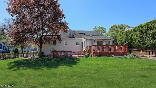 rear view of property with a yard, a deck, solar panels, and a fenced backyard