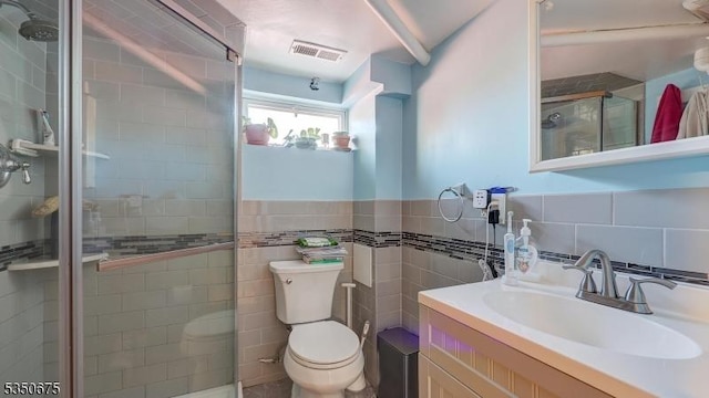 full bath with visible vents, tile walls, a shower stall, vanity, and toilet