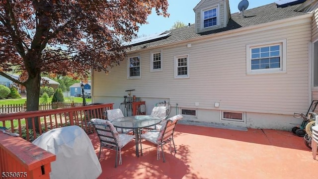 exterior space featuring fence, roof with shingles, outdoor dining space, roof mounted solar panels, and a patio area