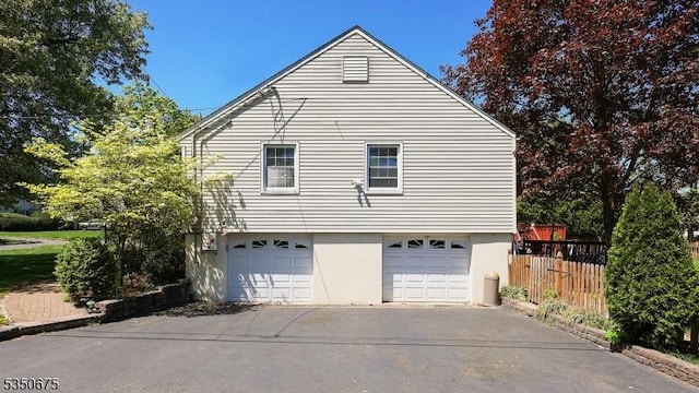 view of home's exterior featuring a garage, fence, stucco siding, and driveway