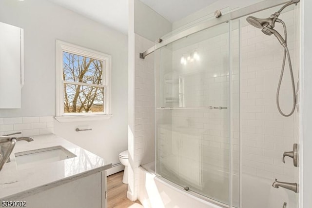 bathroom with vanity, toilet, wood finished floors, a baseboard heating unit, and bath / shower combo with glass door