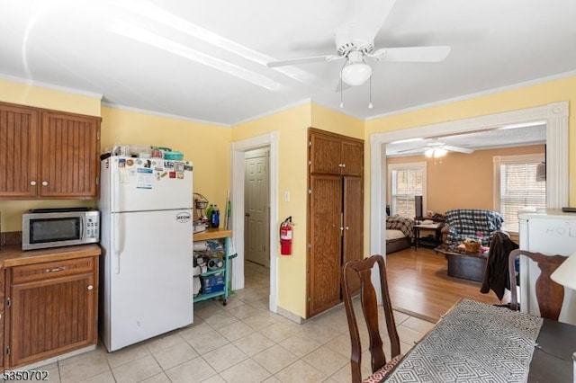 kitchen with stainless steel microwave, freestanding refrigerator, ceiling fan, and light tile patterned flooring