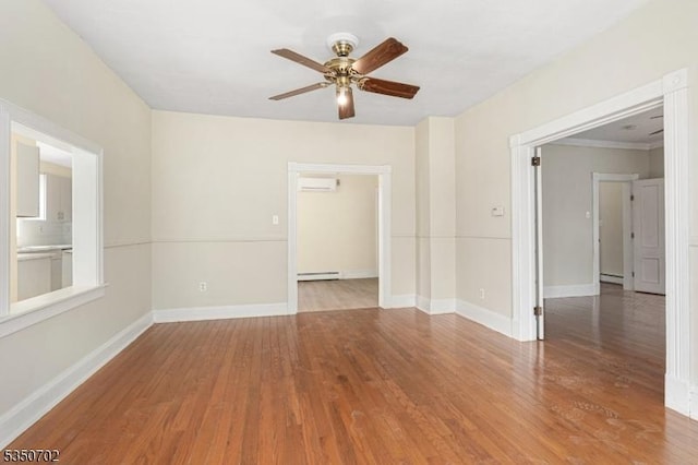 empty room with baseboard heating, wood finished floors, ceiling fan, and baseboards