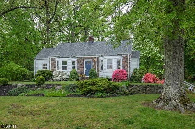 cape cod home with stone siding, a front yard, and a chimney