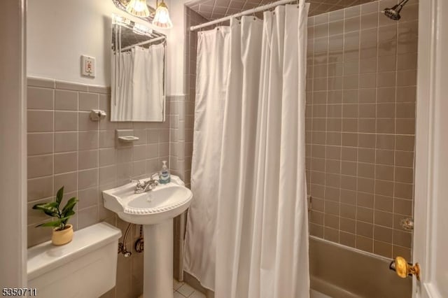 full bath with shower / tub combo, toilet, and tile walls