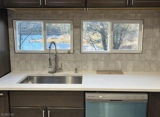 kitchen with light countertops, stainless steel dishwasher, decorative backsplash, and a sink