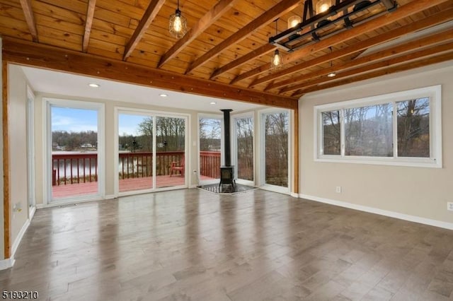 unfurnished living room featuring beamed ceiling, a wood stove, a wealth of natural light, and wood ceiling