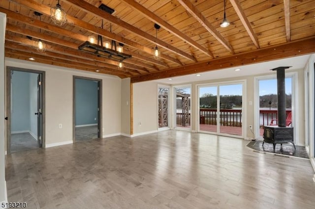 unfurnished living room with wood ceiling, a wood stove, baseboards, beam ceiling, and wood finished floors