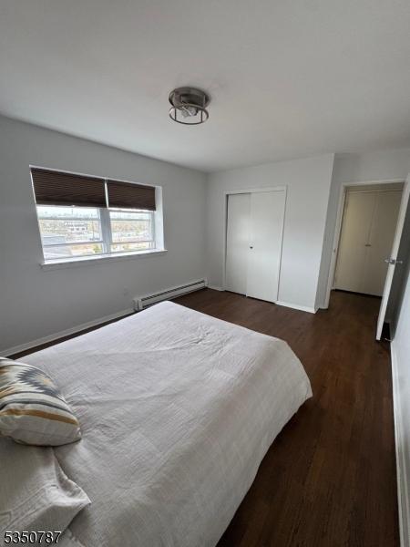 bedroom featuring a baseboard heating unit, wood finished floors, a closet, and baseboards