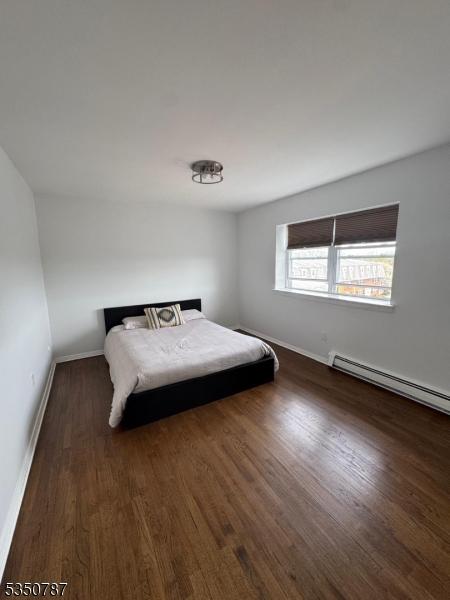 bedroom featuring a baseboard heating unit, baseboards, and wood finished floors