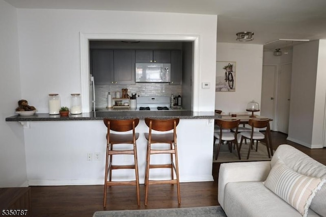 kitchen with a breakfast bar, white range with gas stovetop, dark wood-type flooring, and decorative backsplash