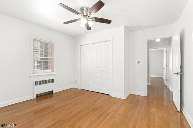 unfurnished bedroom with baseboards, light wood-type flooring, ornamental molding, a closet, and radiator heating unit