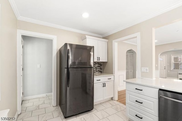 kitchen featuring white cabinets, arched walkways, light countertops, freestanding refrigerator, and crown molding