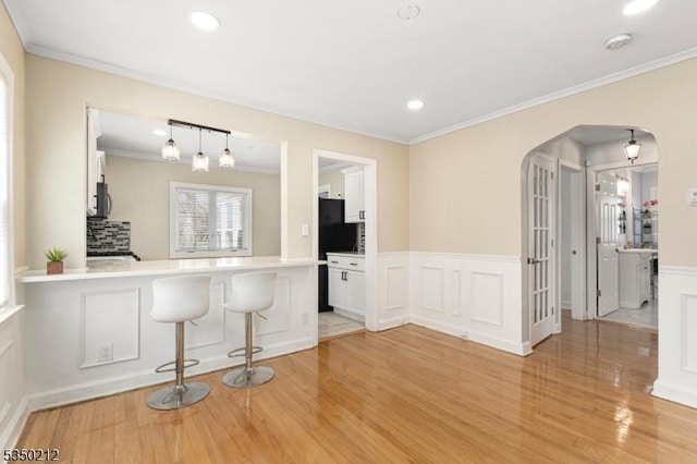 interior space with ornamental molding, stainless steel microwave, arched walkways, and light wood-style floors
