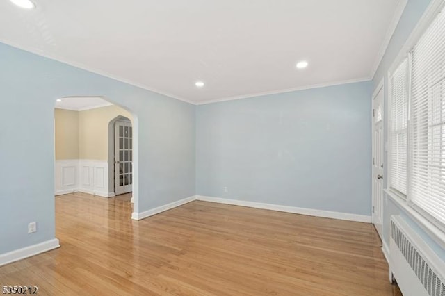 empty room featuring light wood-type flooring, recessed lighting, crown molding, radiator heating unit, and arched walkways
