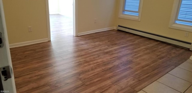 empty room with a baseboard heating unit, wood finished floors, and baseboards