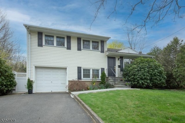 tri-level home featuring an attached garage, aphalt driveway, fence, and a front yard