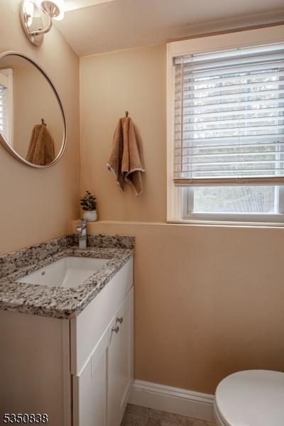 half bath featuring plenty of natural light, baseboards, toilet, and vanity