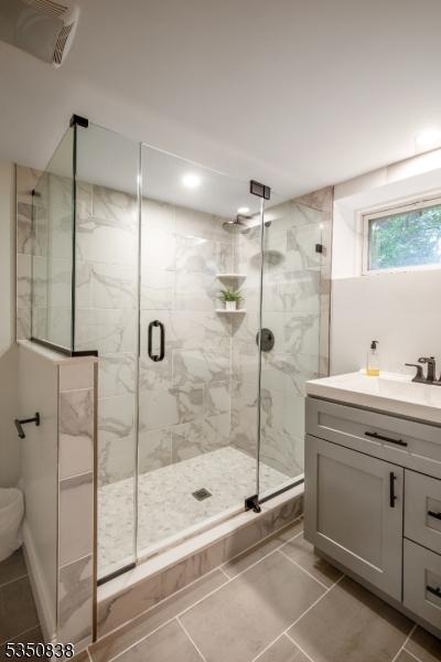 full bathroom with toilet, a marble finish shower, tile patterned flooring, and vanity
