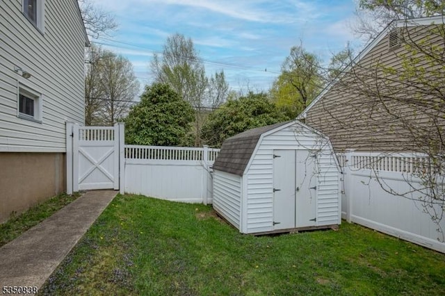 view of yard featuring a storage unit, a fenced backyard, an outbuilding, and a gate