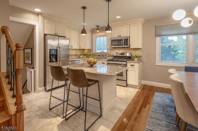 kitchen featuring a kitchen island, backsplash, appliances with stainless steel finishes, light stone countertops, and white cabinetry