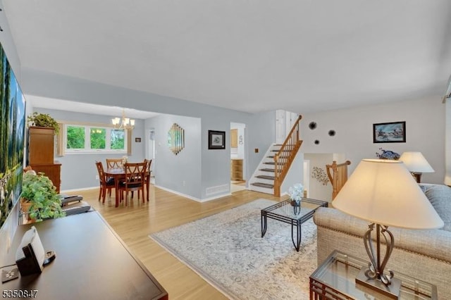 living area featuring light wood finished floors, a chandelier, stairway, and baseboards