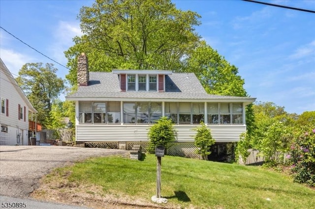 view of front of home featuring a chimney, a front yard, a shingled roof, and a sunroom