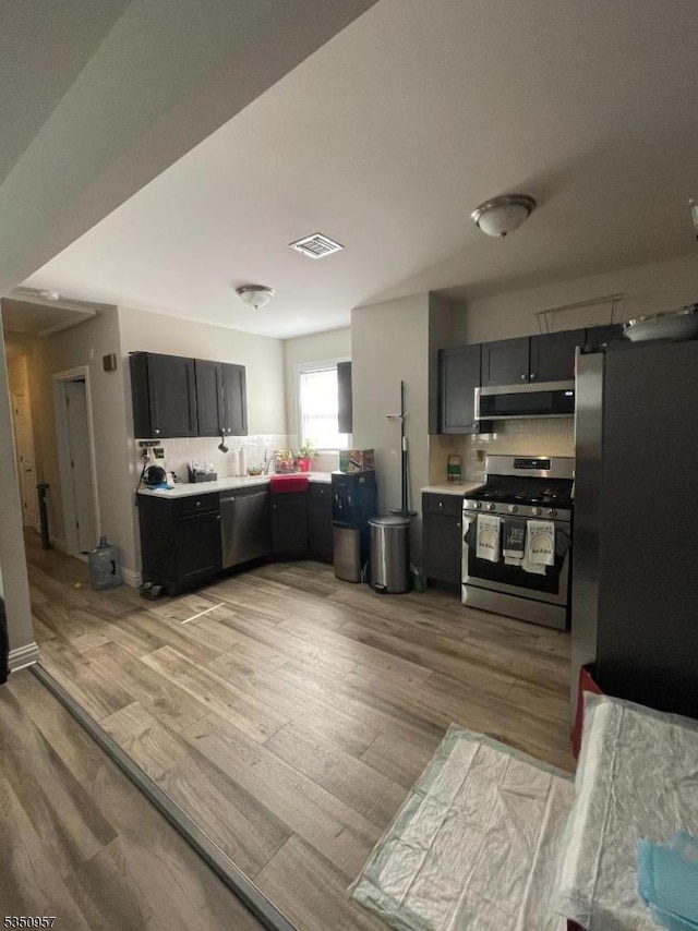 kitchen with light wood finished floors, range hood, light countertops, visible vents, and appliances with stainless steel finishes