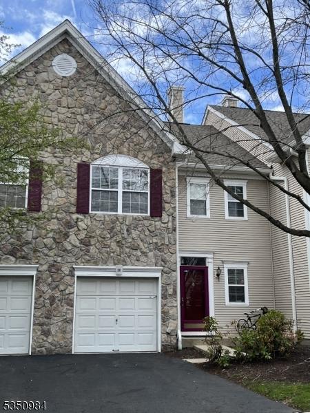 view of property with stone siding, an attached garage, asphalt driveway, and a chimney