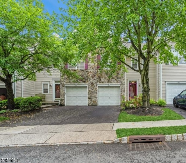 townhome / multi-family property featuring driveway, stone siding, and an attached garage