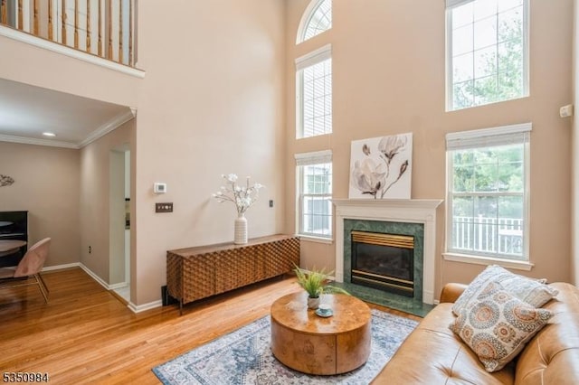 living room featuring a towering ceiling, wood finished floors, ornamental molding, a high end fireplace, and baseboards