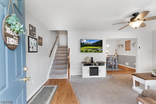 living room featuring stairs, ceiling fan, baseboards, and wood finished floors