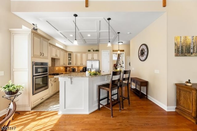 kitchen with appliances with stainless steel finishes, coffered ceiling, light wood-style flooring, and cream cabinetry