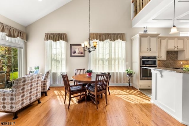 dining room with high vaulted ceiling, an inviting chandelier, and light wood-style floors