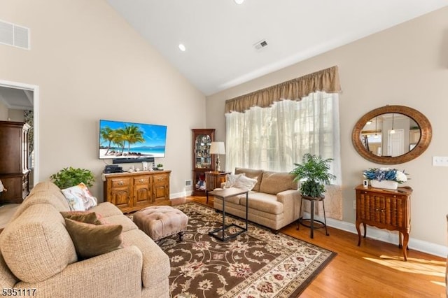living area featuring high vaulted ceiling, baseboards, light wood finished floors, and visible vents