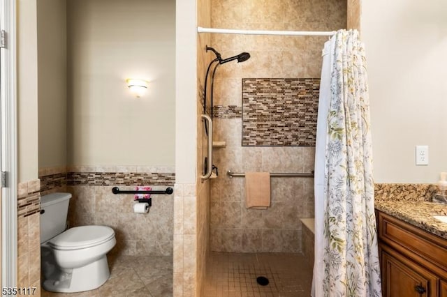 bathroom featuring vanity, toilet, tile walls, a wainscoted wall, and a tile shower