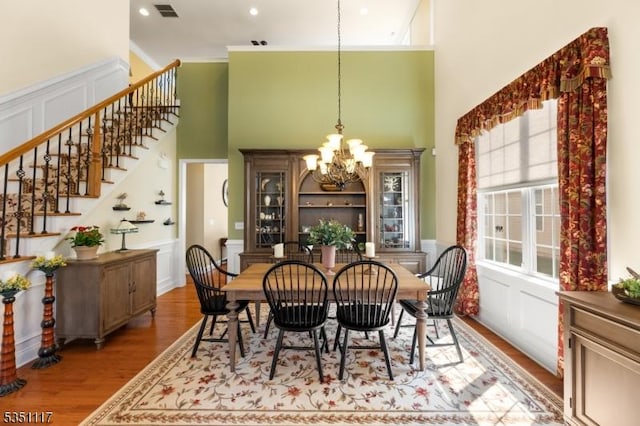 dining area with a chandelier, plenty of natural light, stairs, wood finished floors, and a towering ceiling