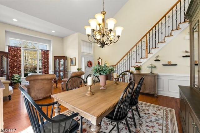 dining area with an inviting chandelier, dark wood finished floors, a wainscoted wall, stairs, and a towering ceiling