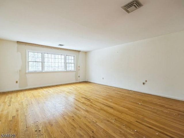 empty room with light wood-type flooring, baseboards, and visible vents