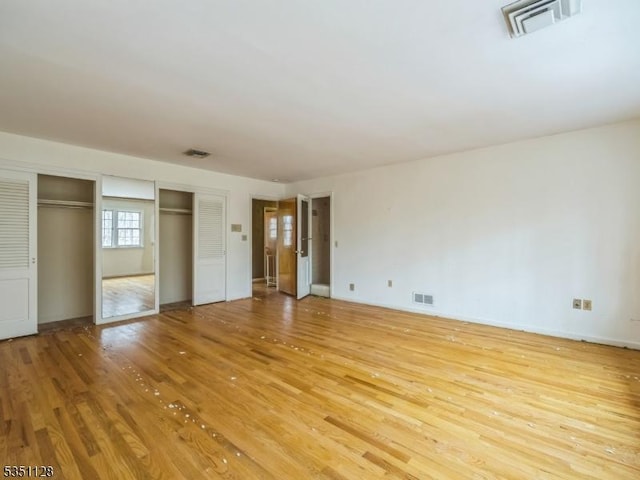 unfurnished bedroom featuring visible vents, light wood-style floors, and two closets