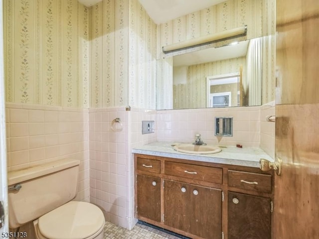 half bathroom featuring tile walls, wallpapered walls, a wainscoted wall, and toilet