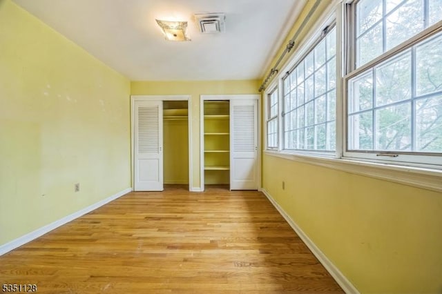 unfurnished bedroom with two closets, visible vents, baseboards, and light wood-type flooring
